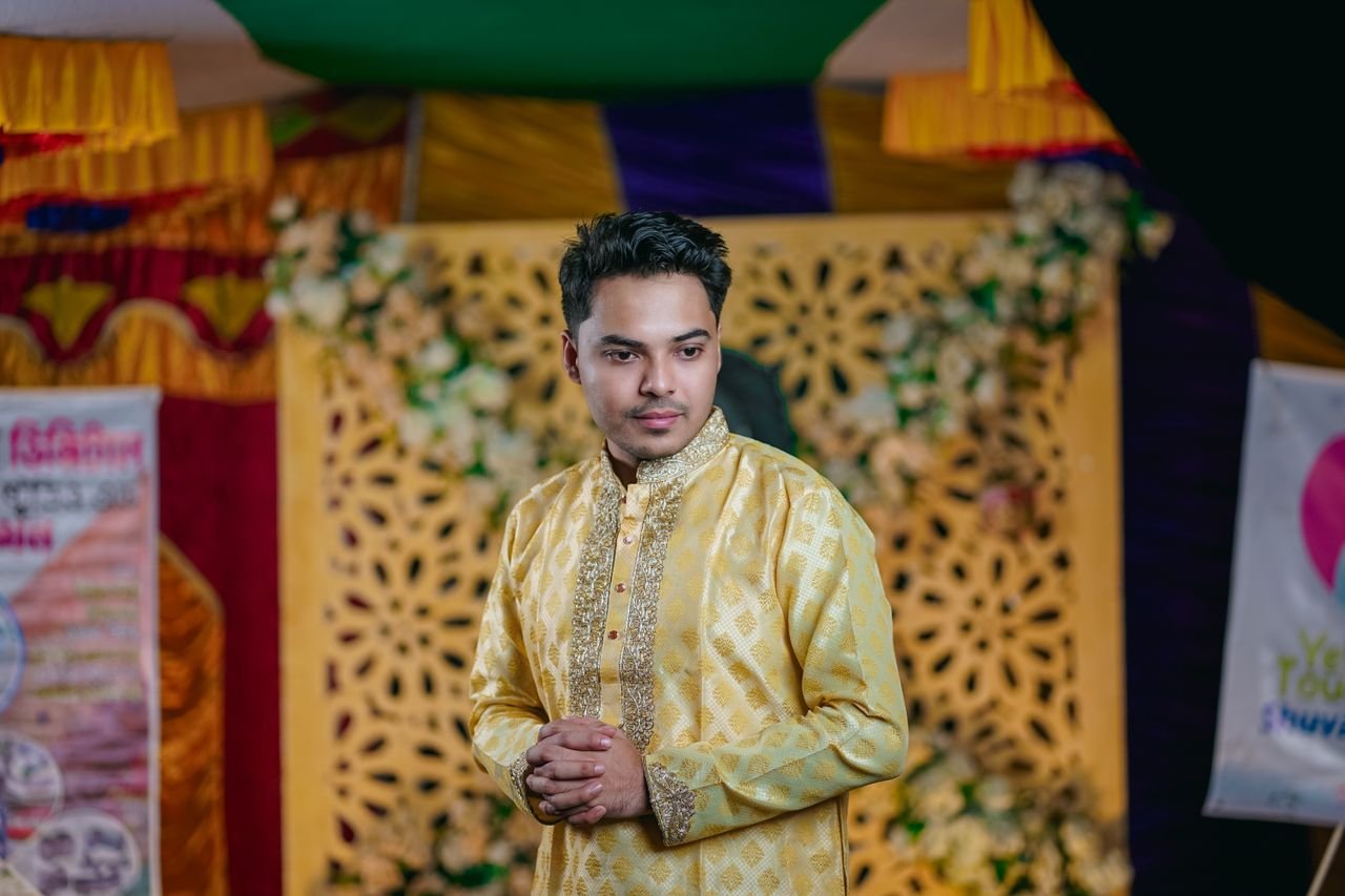 Elegant man in traditional attire at a vibrant indoor celebration in Bangladesh.